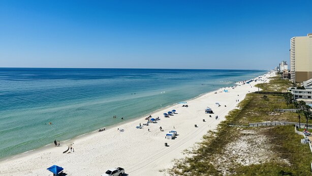 A beach with clear blue water, a sandy shore, and a few umbrellas. There are buildings adjacent to the beach. - FREE Beach Service!  Endless View 702 - New Listing (Panama City Beach)