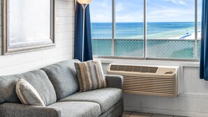 A room with a gray sofa, a framed picture, a window with a view of the ocean and a pier, and a standing lamp. - FREE Beach Service!  Endless View 702 - New Listing (Panama City Beach)