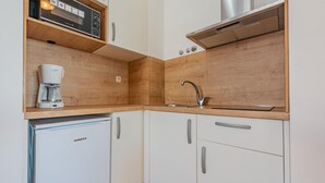 Een compacte keuken met witte kastjes, een Bosch koffiezetapparaat, een roestvrijstalen spoelbak en een Koncar koelkast.