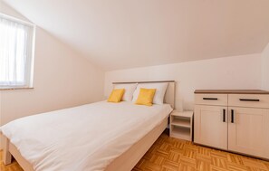 A bedroom with a bed, two yellow pillows, a nightstand, a wooden wardrobe, and a window with sheer curtains. - Beach front apartment in Kosljun with WiFi (Kosljun)