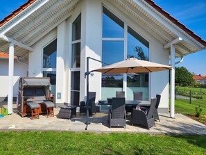 A modern house with a patio area featuring wicker furniture, a table, and an umbrella.