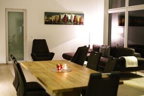 Een eethoek met een houten tafel, stoelen en een schilderij van zeilboten aan de muur.