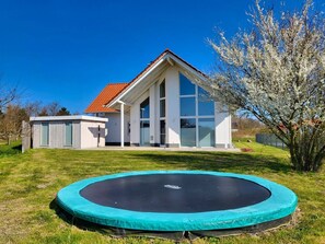 A modern house with a large glass window, a red roof, and a trampoline in the yard.
