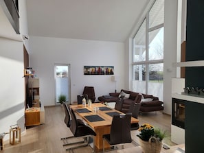 Una sala de estar moderna con una gran mesa de comedor, asientos cómodos, una chimenea y un ventanal que ofrece vistas al exterior.