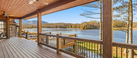 A wooden deck with a railing overlooking a lake, a ceiling fan, and a clear view of the surrounding landscape.