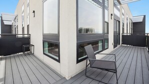 En moderne bygning med store vinduer, en træterrasse og en metalstol.