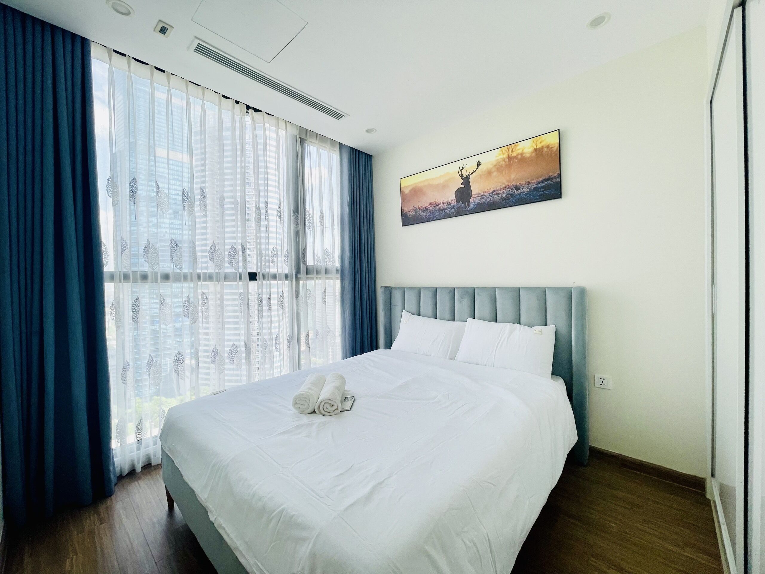 Een hotelkamer met een groot bed, een hoofdbord, een raam met dunne gordijnen en een schilderij aan de muur.