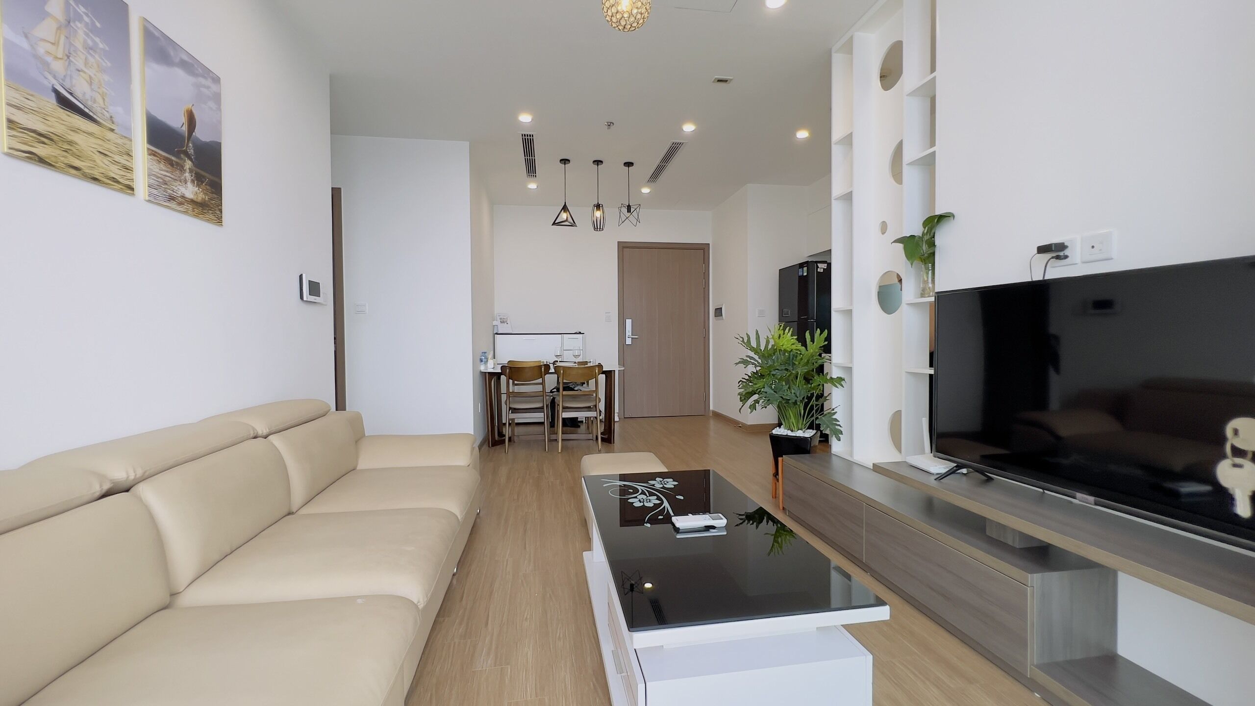 A modern living room with a sofa, a coffee table, a TV, and a dining area with chairs and a table.