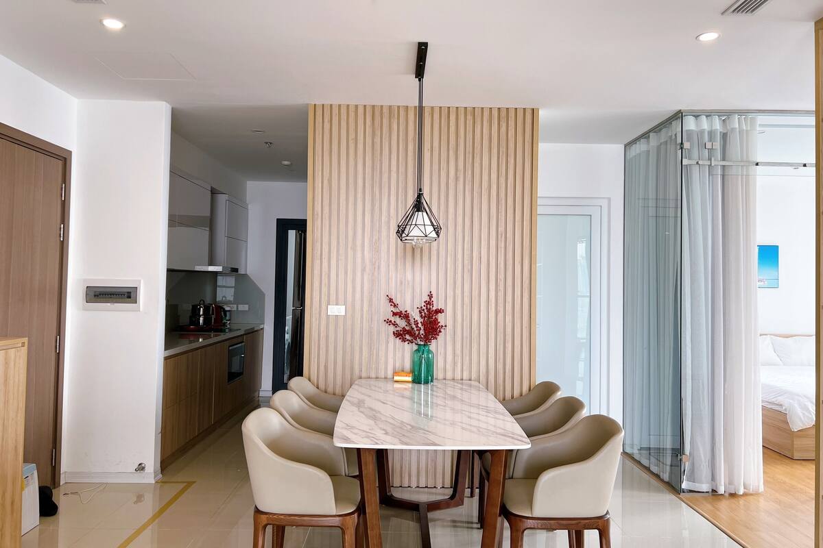 A modern dining area with a marble table, leather chairs, a pendant light, and a vase with red flowers.