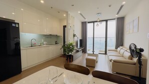 Un apartamento moderno con cocina, comedor y sala de estar. Cuenta con un ventanal con vistas a la ciudad, un refrigerador negro y un sofá color beige.