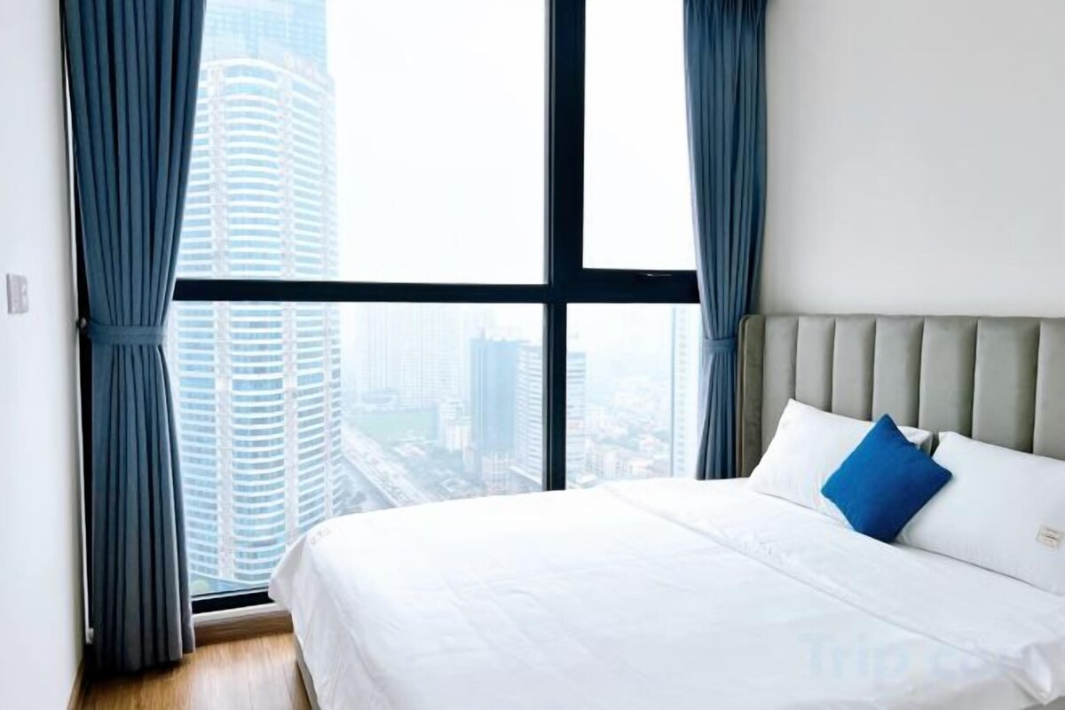 Habitación de hotel con un ventanal grande, cama con ropa de cama blanca y vista a la ciudad.