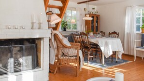 Ein gemütlicher Essbereich mit Kamin, Korbstühlen, einem Holztisch und Blick ins Freie.