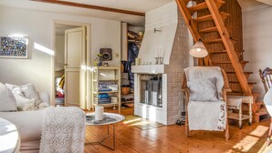 Ein gemütliches Wohnzimmer mit Kamin, einer Holztreppe und einem Korbsessel.