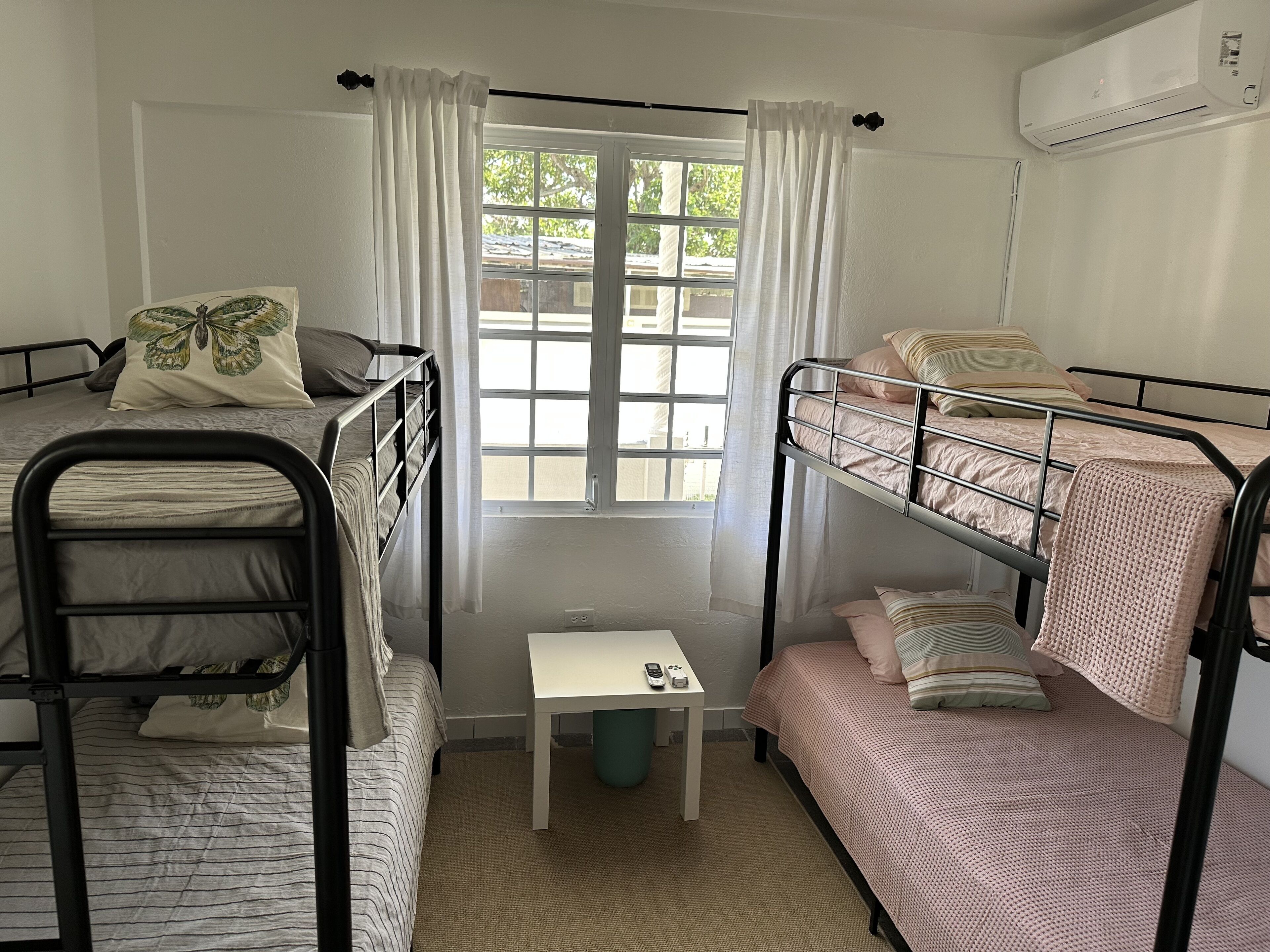 A dormitory room with bunk beds, a small table, and a window with curtains.