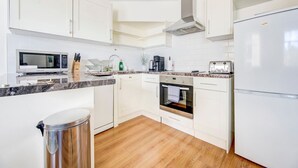 A modern kitchen with white cabinets, a stainless steel range hood, a built-in oven, a microwave, and a refrigerator.