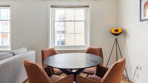 A room with a round table and chairs, a floor lamp, a sofa, and a window with blinds.
