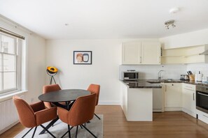Une cuisine compacte avec des meubles blancs, un four à micro-ondes, un évier et un coin repas comprenant une table et des chaises.