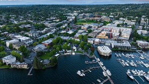 Vue aérienne d’une ville côtière, avec un port de plaisance, un centre urbain dense et une végétation luxuriante environnante.