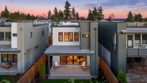 Une maison moderne à plusieurs étages, dotée d’un patio couvert et offrant une vue sur la forêt environnante.