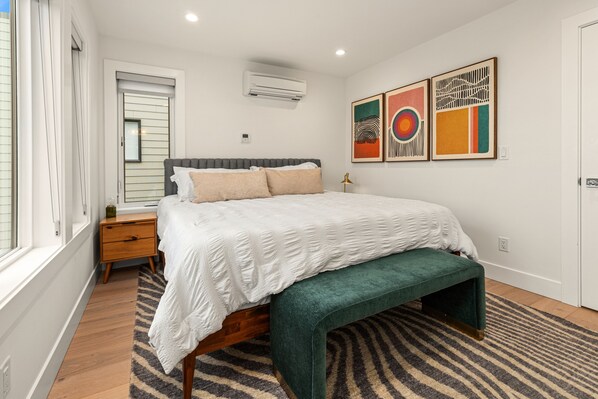 A bedroom with a bed, a bench, a nightstand, a window, and artwork on the wall. - Unobstructed, Breathtaking Water Views RIGHT in Kirkland, WA. (Kirkland)