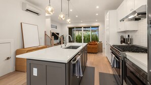 Une cuisine moderne dotée d’un îlot central, d’appareils électroménagers en acier inoxydable et de luminaires suspendus.