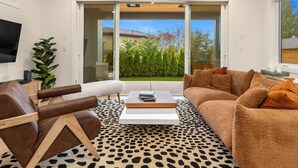 Un salon moderne comprenant un canapé, un fauteuil et une table basse, un téléviseur à écran plat et une porte-fenêtre coulissante donnant sur un jardin.