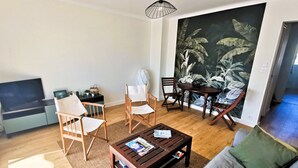 En stue med en sofa, to lænestole, et sofabord, et fjernsyn, et maleri og et spisebord med stole.