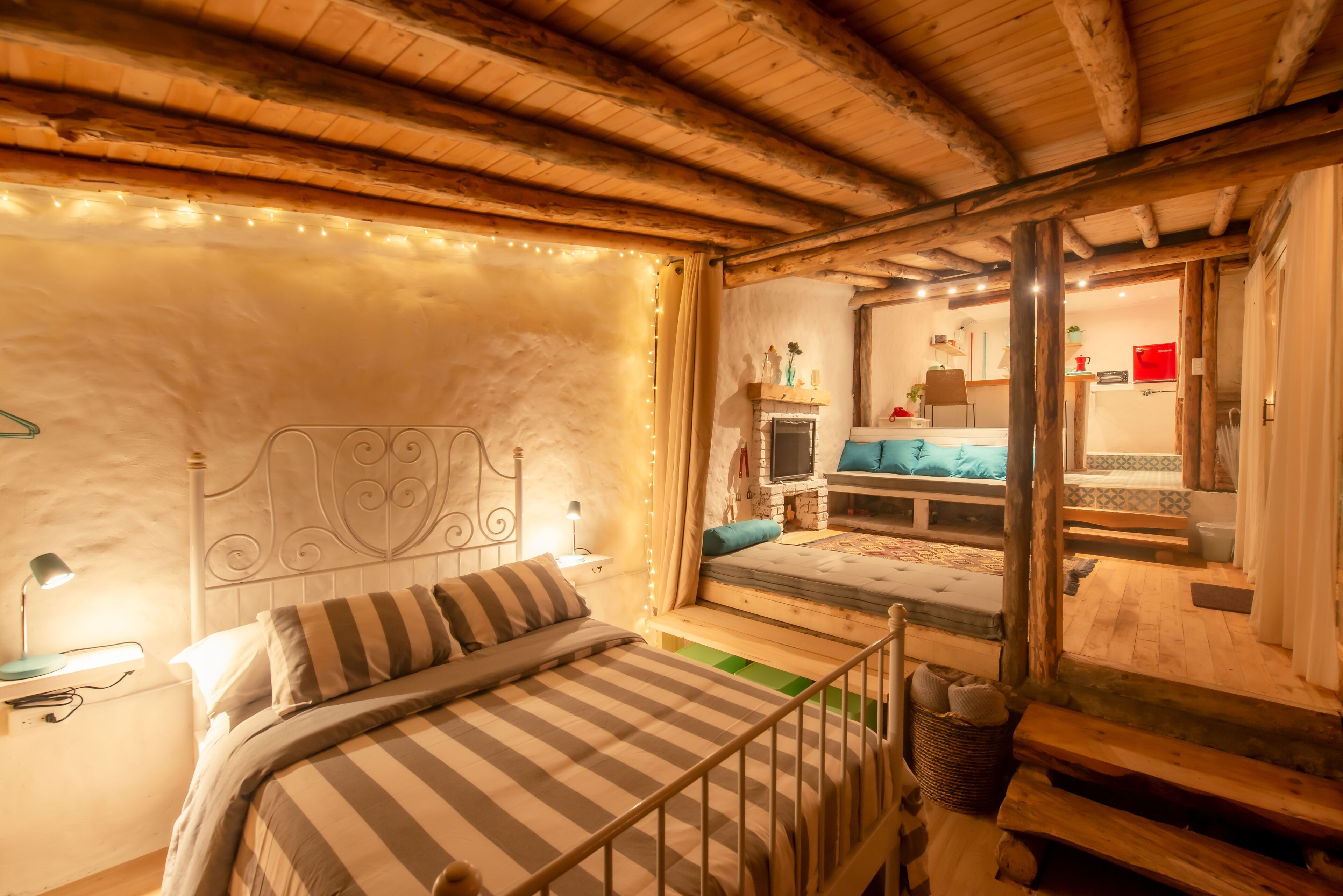 Quarto aconchegante com teto de madeira, cama com roupa de cama listrada, mesa de cabeceira e uma pequena janela.