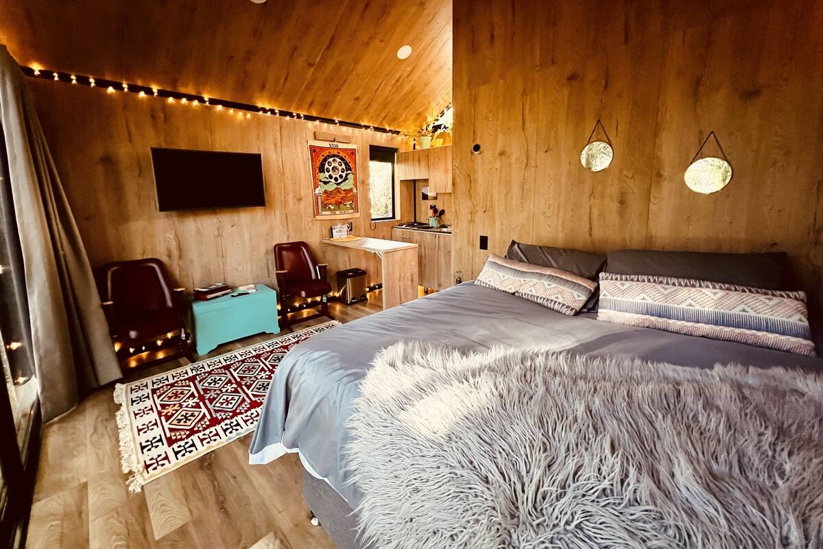 Een gezellige slaapkamer met een houten plafond, een bed met opvallende kussens, een bureau met stoel en een aan de muur bevestigde televisie.