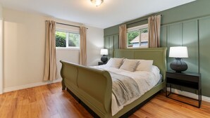 Un dormitorio con una cama tapizada de verde, dos mesitas de noche con lámparas, una ventana con cortinas y una lámpara de techo.