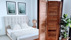A bedroom with a bed, a wooden wardrobe, a round table, and two framed pictures on the wall. - Apartamento Moderno y Confortable con Piscina Comunitaria (Verger)