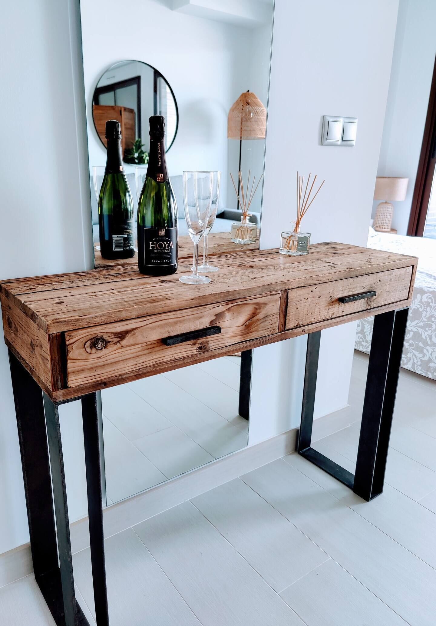 A wooden desk with two drawers, a wine bottle, and two glasses.