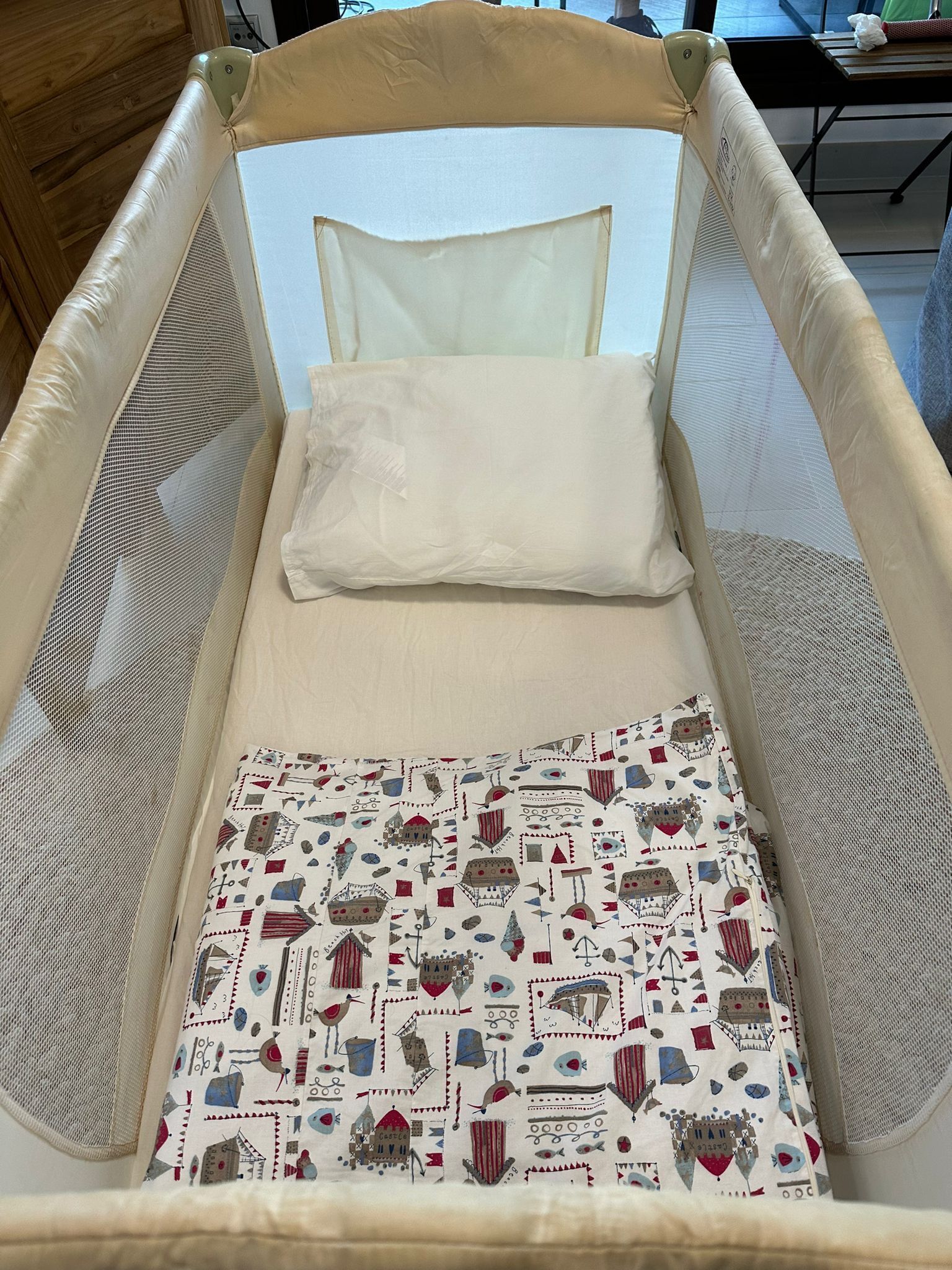 A baby crib with a mesh enclosure and a patterned pillow.