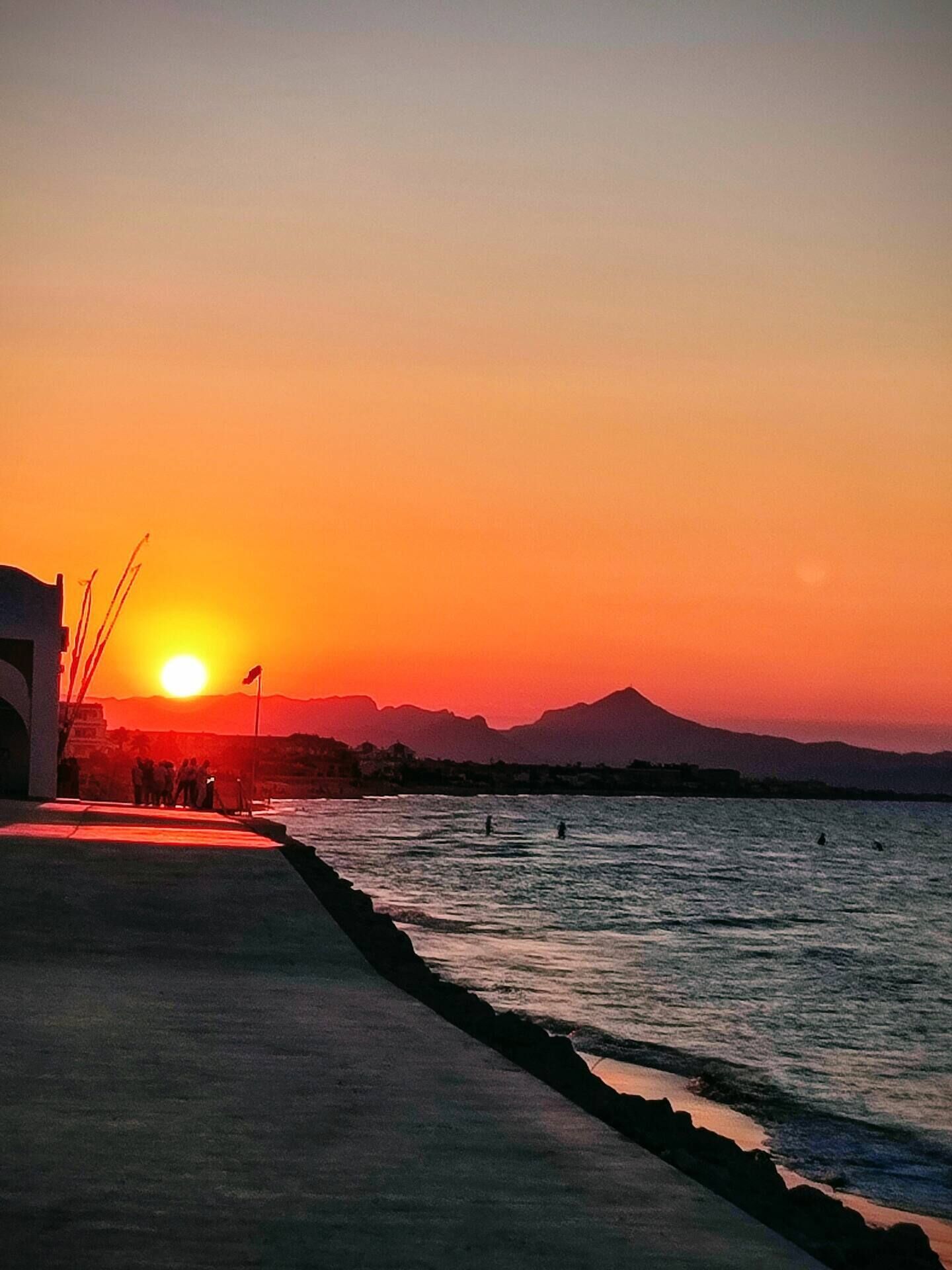 A sunset over a body of water with a concrete walkway and distant mountains.