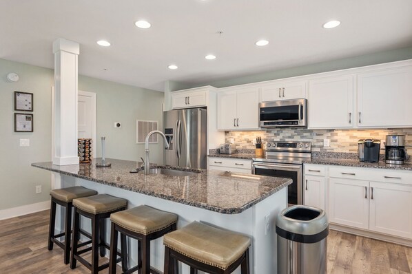 A modern kitchen with white cabinets, granite countertops, stainless steel appliances, and bar stools.