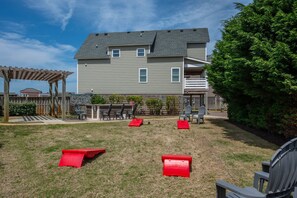 A backyard with a wooden pergola, a barbecue area, and a fenced play area with red play structures.
