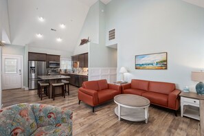 A modern kitchen with stainless steel appliances, a dining area with a red sofa and a round coffee table, and a living room with a large painting.