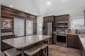 A modern kitchen with a granite countertop, stainless steel appliances, and wooden paneling on the walls.