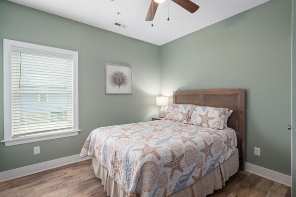 A bedroom with a bed, a ceiling fan, a window with blinds, and a wall-mounted picture.