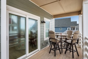 A covered outdoor seating area with a table and chairs, a sliding glass door, and a view of a neighboring house.