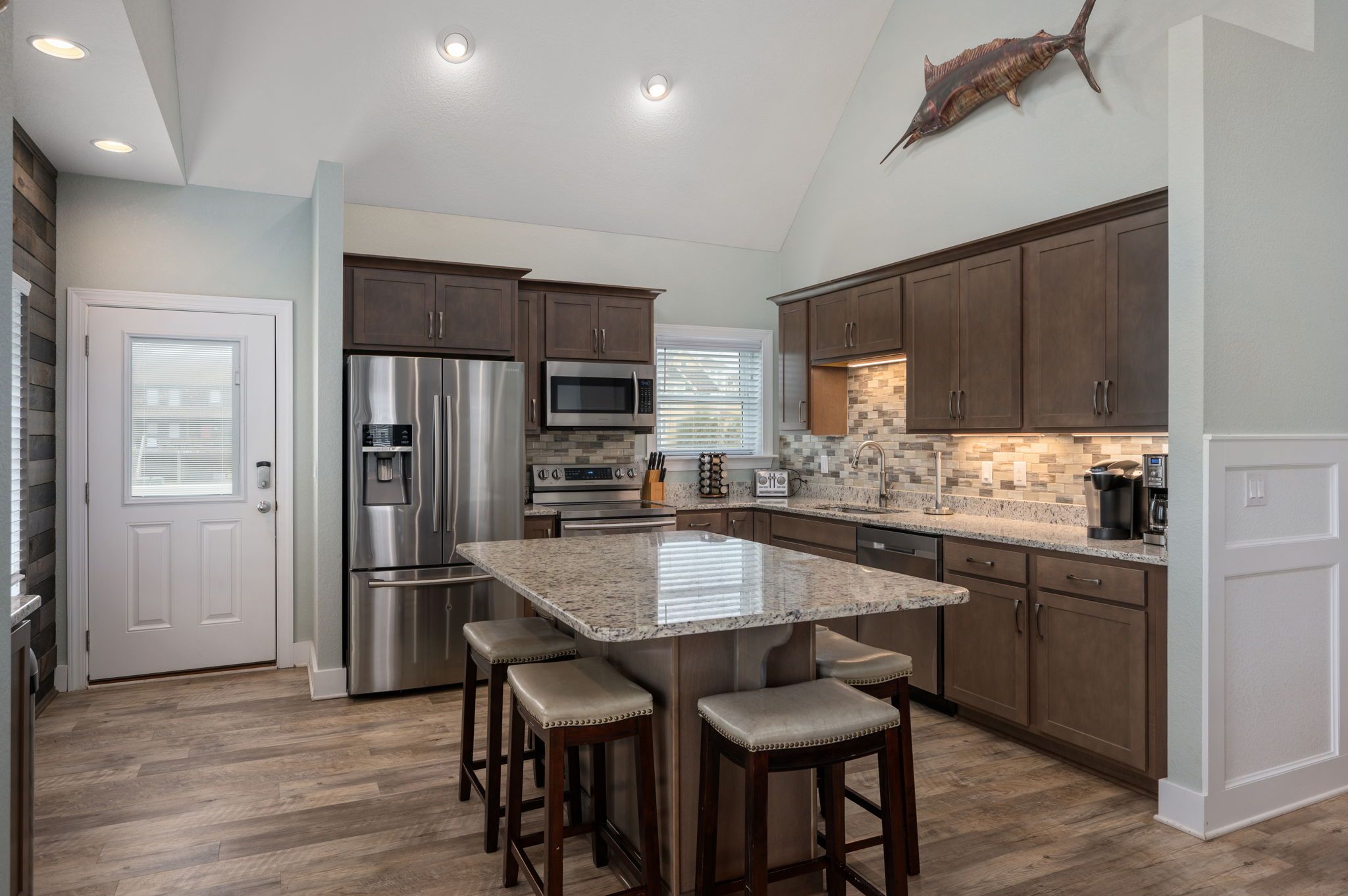 A modern kitchen with a central island, stainless steel appliances, and a decorative fish on the wall.