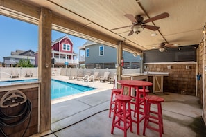 A covered outdoor area with a pool, red bar stools, and a ceiling fan.