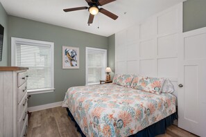 A bedroom with a bed, a ceiling fan, a dresser, a nightstand, and a door. - Bodie Island Cottage: Semi-Oceanfront, Hot tub and Community Pool (Nags Head)