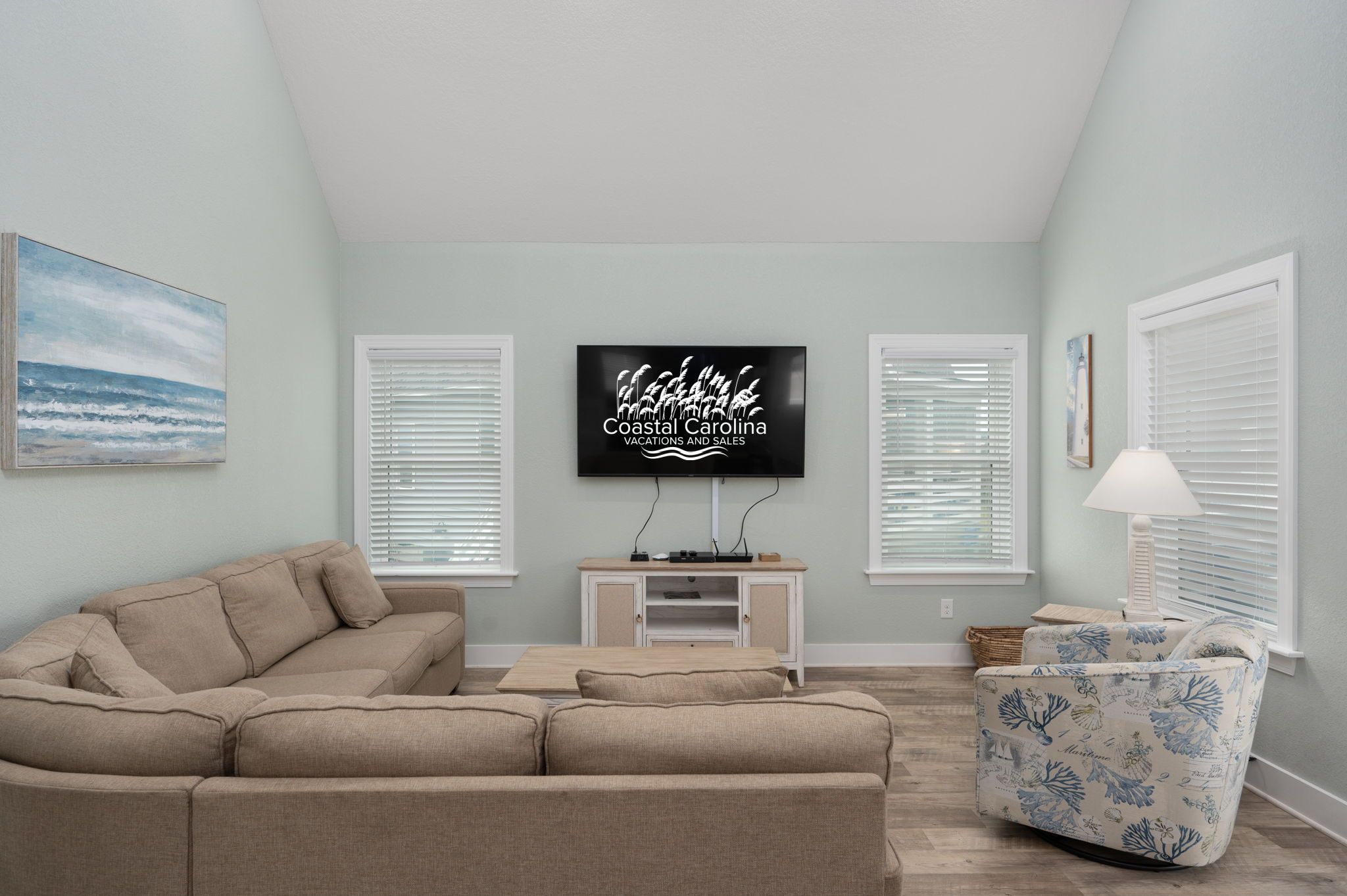 A living room with a beige sectional sofa, a flat-screen TV on a stand, and a patterned armchair.