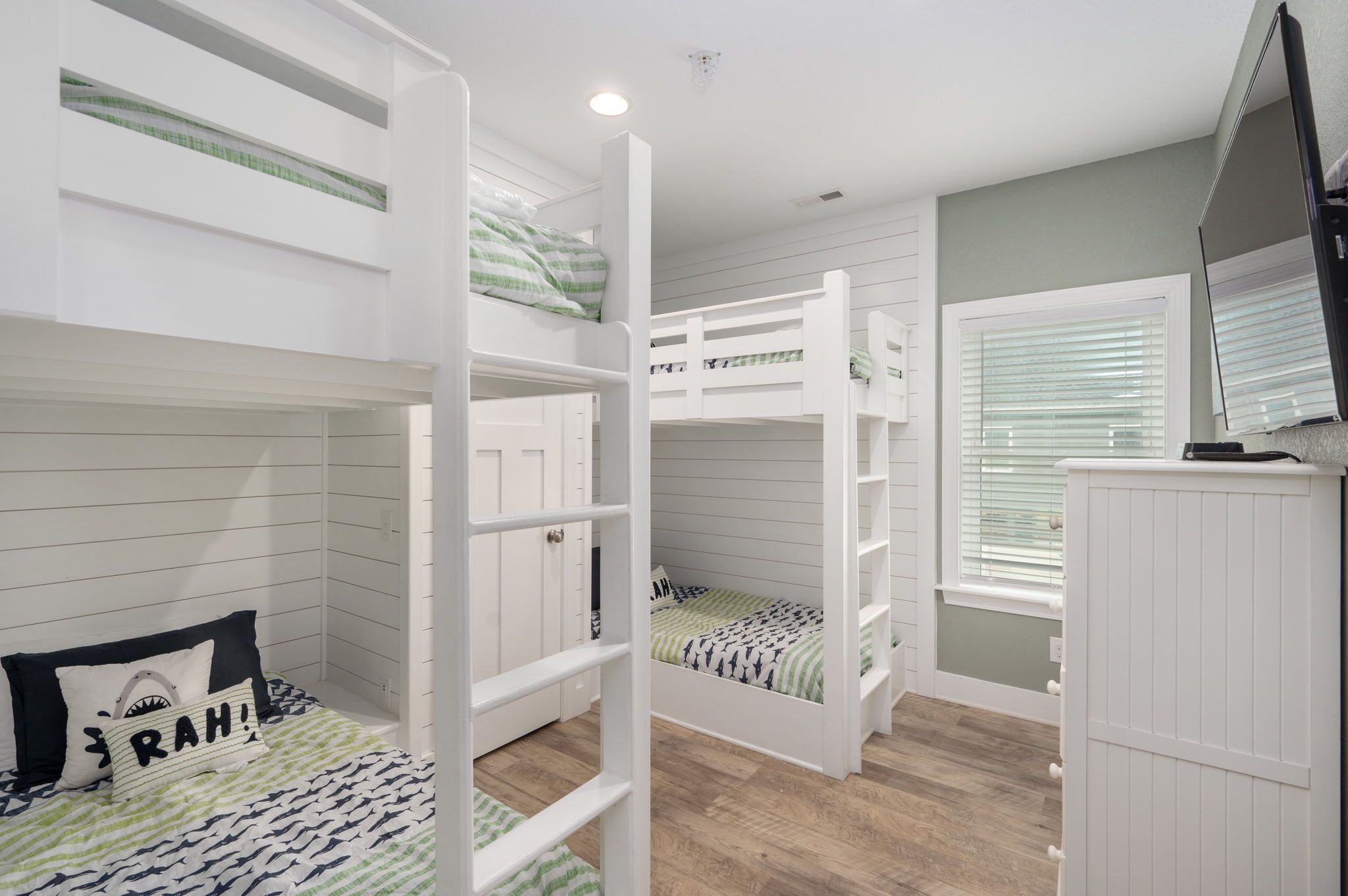 A bunk bed room with a white wardrobe, a window with blinds, and a ceiling light.