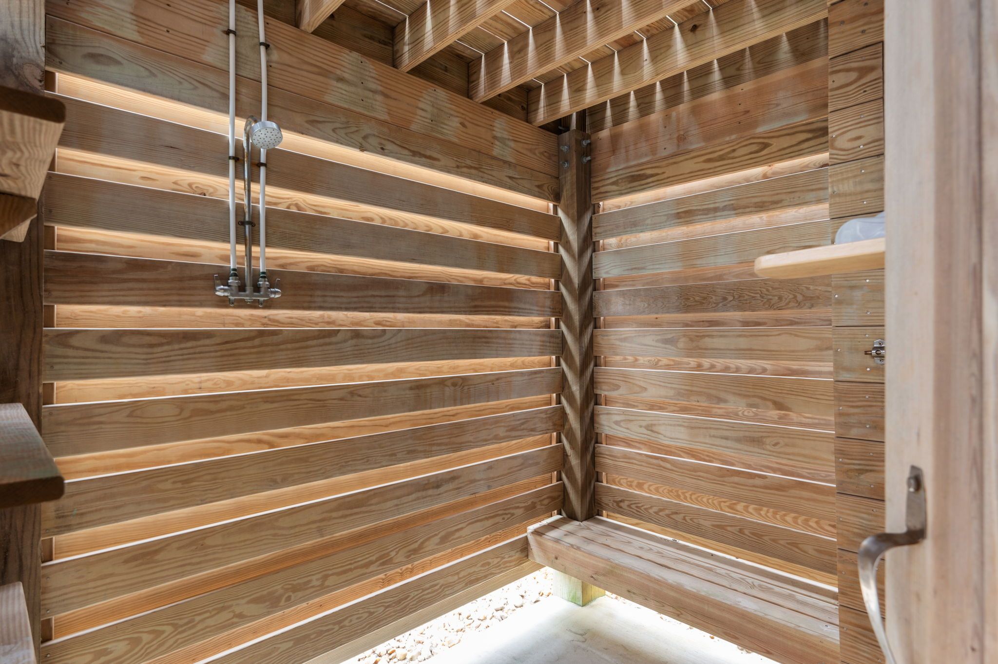 A wooden interior with horizontal slats, a showerhead, and a door.
