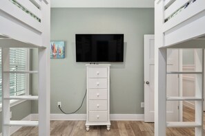 A room with a television mounted on the wall, a white dresser, and a painting of sailboats. - Ocracoke Cottage: Semi-Oceanfront, Hot Tub, Close walk to the Beach (Nags Head)