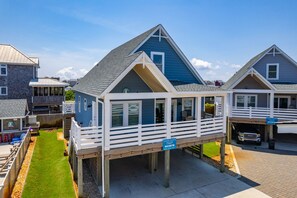 A coastal house with a deck, a sign indicating it's a vacation rental, and a paved walkway.