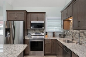 A modern kitchen with stainless steel appliances, granite countertops, and wooden cabinetry.