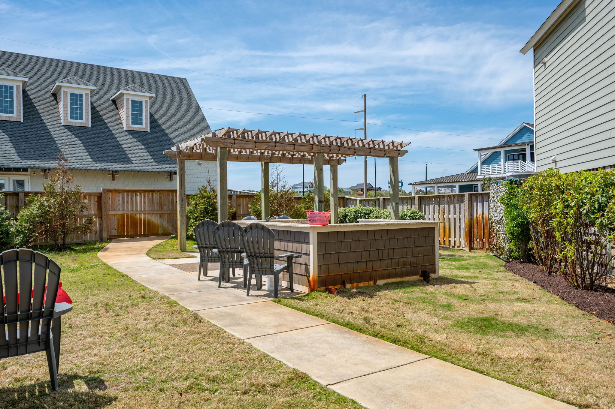 Un patio trasero con una pérgola de madera, zona de barbacoa y un conjunto de asientos.